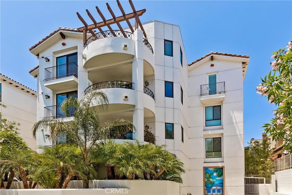 Front view of a multi-story building with balconies and a pergola on the roof.