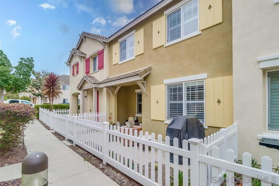 Front view of a two-story house with a fenced patio and shutters.