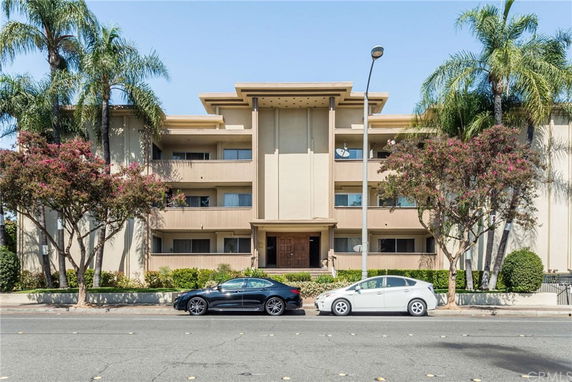 Front view of a multi-story residential building with balconies and palm trees.
