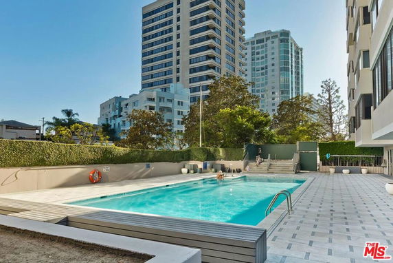 Outdoor swimming pool area with tall buildings in the background.