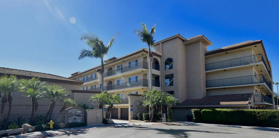 Front view of a multi-story building with balconies and palm trees.