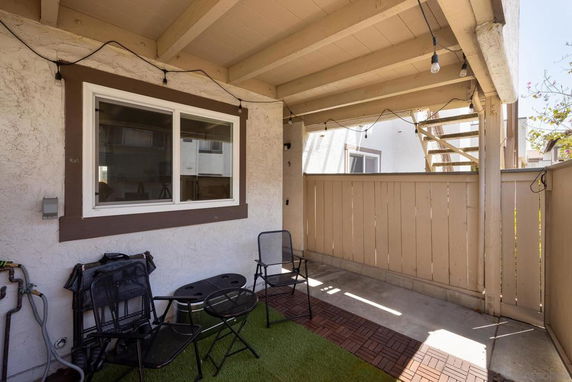 Covered patio area with chairs and a table next to a window.
