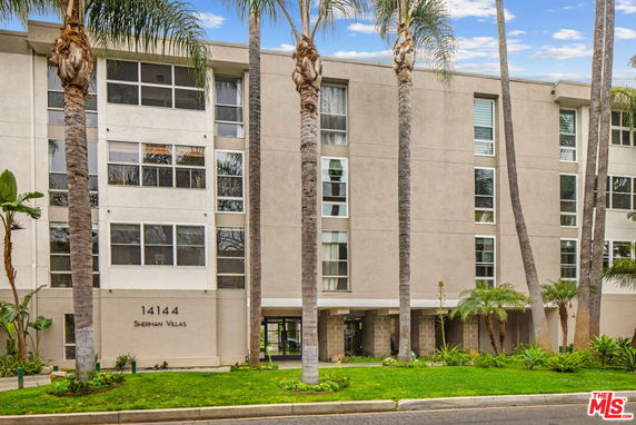 Front view of a multi-story building with large windows and palm trees in front.
