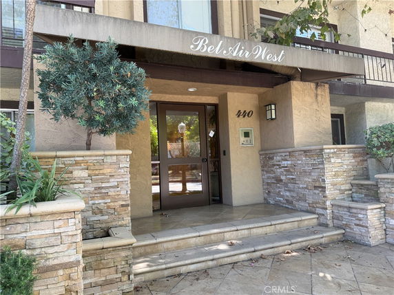 Front view of a multi-story building entrance with stone accents and plants.