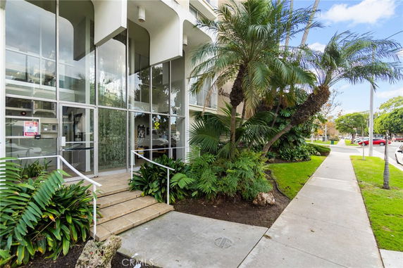 Front view of a building entrance with glass doors and plants.