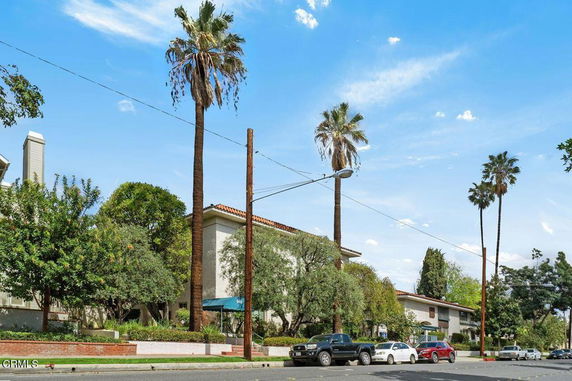 Front view of a residential building with palm trees and parked cars.