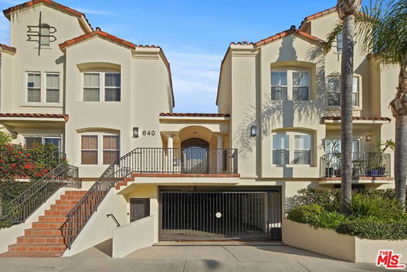 Front view of a multi-story residential building with staircases leading to the main entrance and a gated garage.