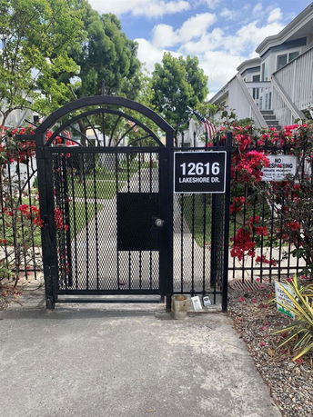 Front view of a metal gate entrance with house building in the background.