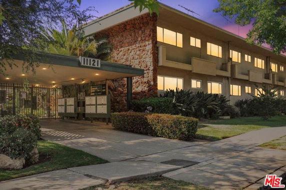 Front view of a multi-story apartment building with a covered entrance and lush landscaping.