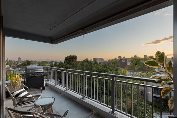 Balcony with outdoor seating and view of city skyline at sunset.