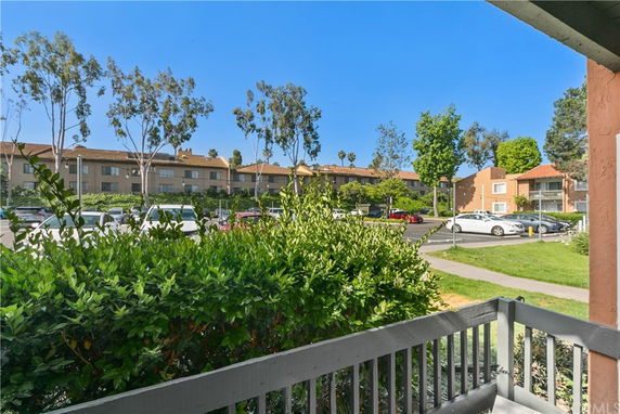 View of a parking area with cars and adjacent apartment buildings, seen from a porch.