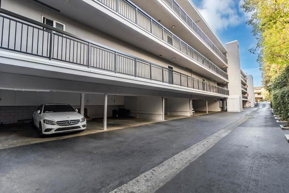 Outdoor parking area under a multi-story building with covered parking spaces.