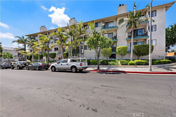 Front view of a multi-story apartment building with balconies and palm trees.