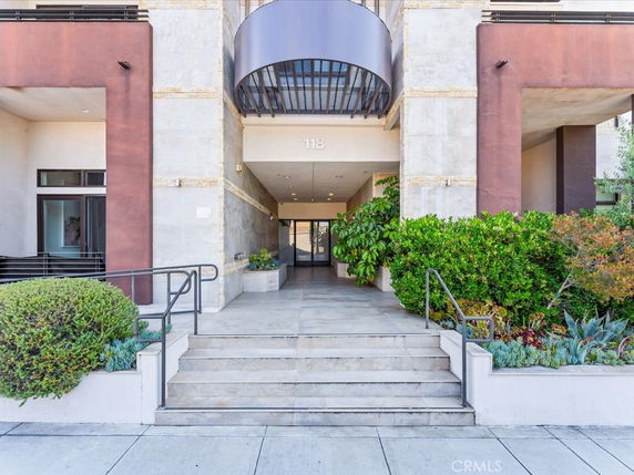 Entrance of a modern multi-story building with stairs and plants.
