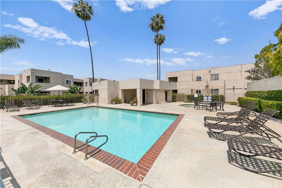 Outdoor swimming pool area with surrounding buildings and palm trees.