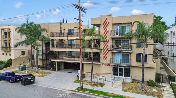Front view of a multi-story apartment building with balconies and palm trees.