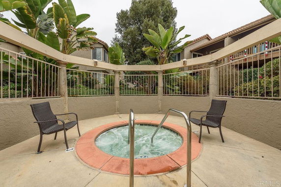 Outdoor area with a circular hot tub, surrounded by a fence and two chairs.