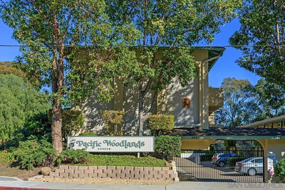 Front view of a multi-story condominium building with a parking area at the entrance.