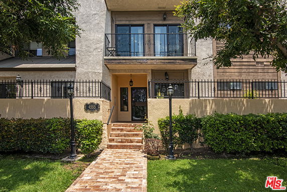 Front view of a multi-story building with a balcony and a brick pathway.