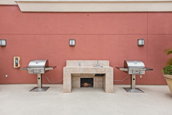 Outdoor patio with two stainless steel grills and a tiled counter with a sink against a red wall.