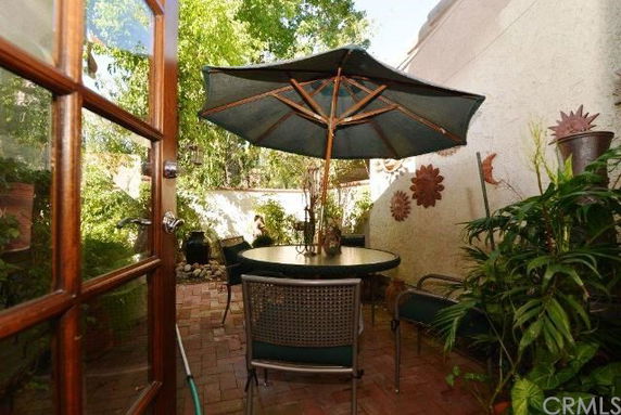 Outdoor patio area with a table, chairs, and a large umbrella, surrounded by plants and walls.