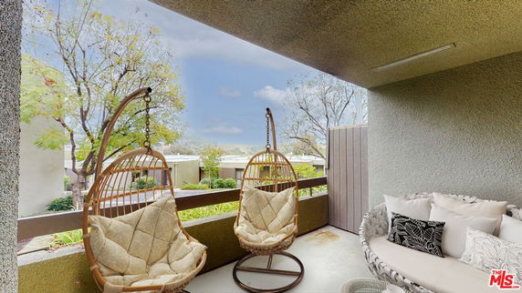 Covered balcony with hanging chairs and a view of trees and neighboring buildings.