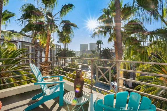 Outdoor balcony with chairs overlooking palm trees and a distant view of buildings.