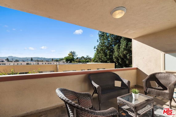 Outdoor patio with wicker furniture overlooking surrounding buildings and trees.