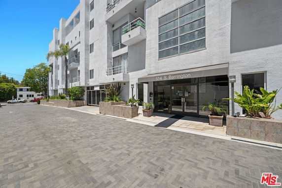 Front view of a multi-story residential building with balconies and potted plants at the entrance.