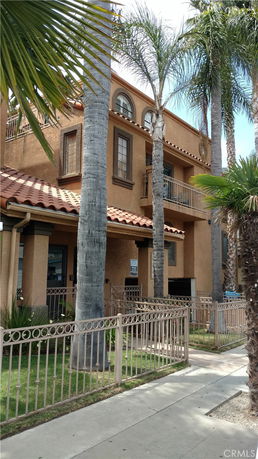 Front view of a multi-story house with a balcony and palm trees.