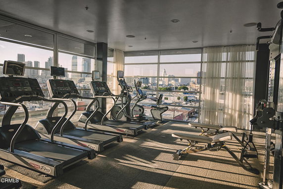 Indoor gym area with treadmills and exercise equipment, large windows providing city view.