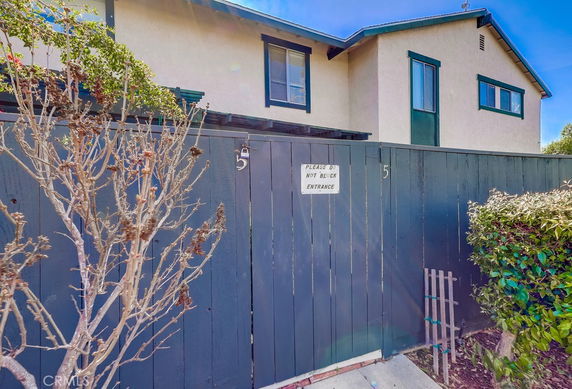 Front view of a two-story house with a tall fence and plants.