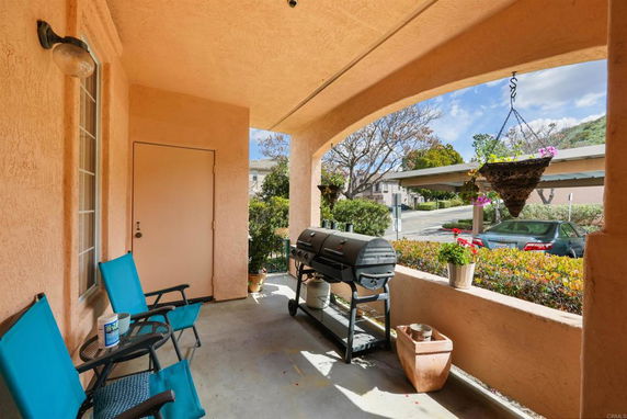 Patio area with a barbecue grill and outdoor chairs, overlooking a parking area and street.