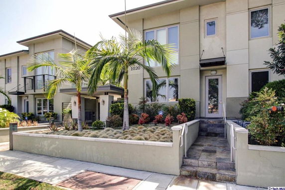 Front view of a modern two-story house with a small entrance staircase and surrounding greenery.
