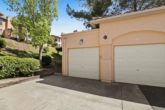 Outdoor view of a double garage with white doors and beige walls, surrounded by trees and shrubs.