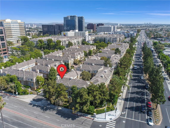 Aerial view of a residential complex with multiple buildings surrounded by trees, located near a busy road.