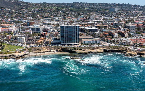Aerial view of a coastal cityscape with a prominent tall building near the shoreline.