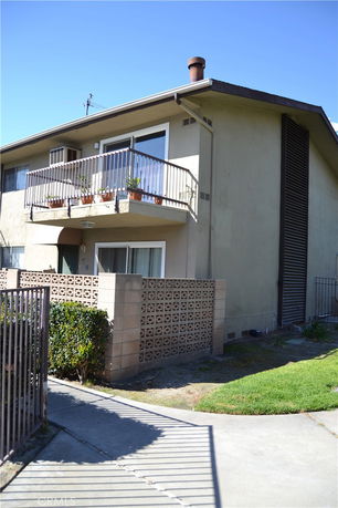 Front view of a two-story house with a balcony and brick wall fencing.