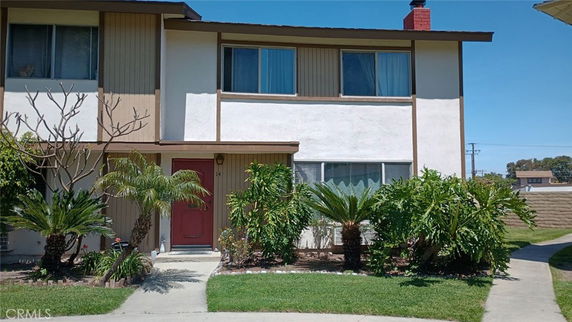 Front view of a two-story house with a red door and surrounding greenery.