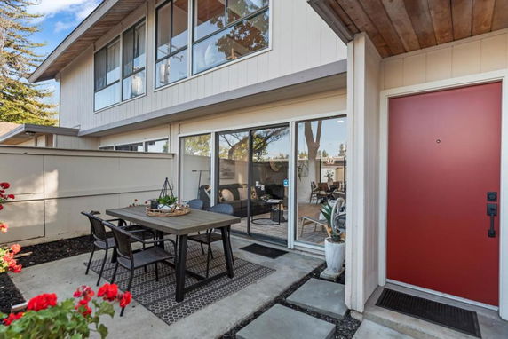 Front view of a two-story house with a red door and outdoor dining area.