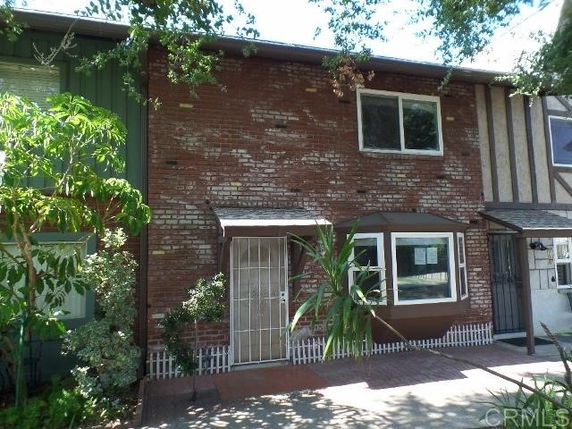 Front view of a two-story brick townhouse with a metal security door and plants around the entrance.