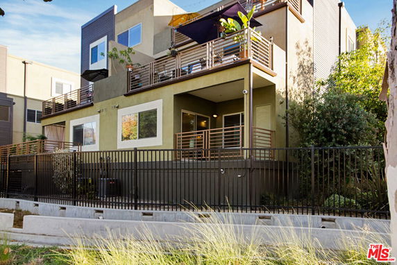 Front view of a multi-story building with a balcony and a fenced yard.