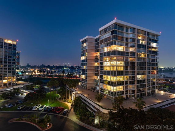Evening view of a multi-story residential building with city lights in the background.