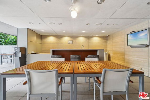 Interior view of a modern clubhouse with a wooden table and chairs, a wall-mounted TV, and a countertop area.