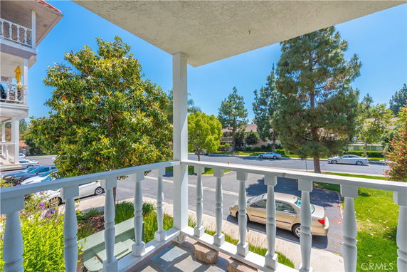 View from a house balcony overlooking a street with trees and parked cars.