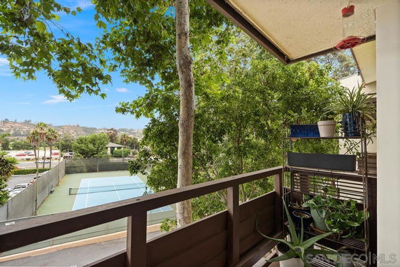 View from a balcony overlooking a tennis court and surrounding greenery.