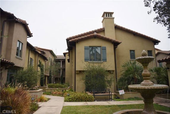 Front view of a two-story house with a central chimney and a fountain in the foreground.
