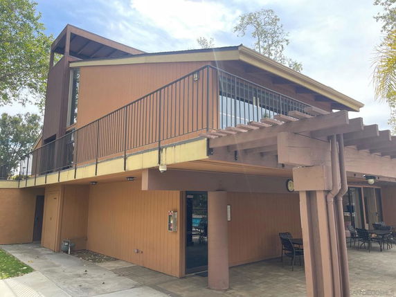 Front view of a two-story building with wooden panels and railing.