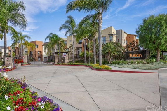 Entrance view of a modern residential complex with palm trees and a gated entry.
