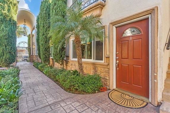 Front view of a house with a red door and arched entrance, surrounded by tall trees and plants.
